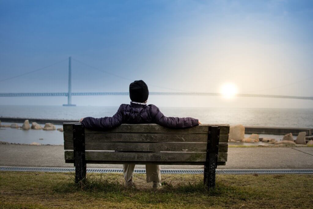 person sitting on bench facing suspension bridge