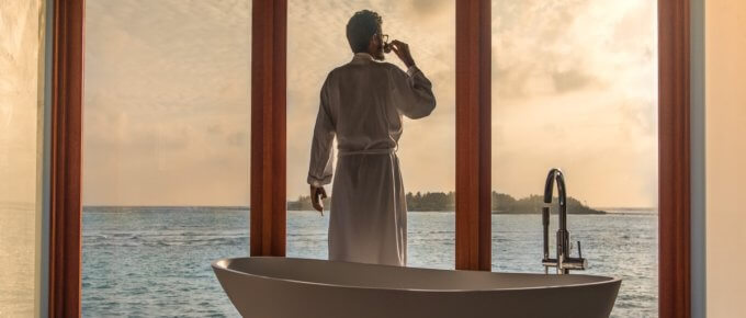 man standing in bathroom with bathtub next to body of water