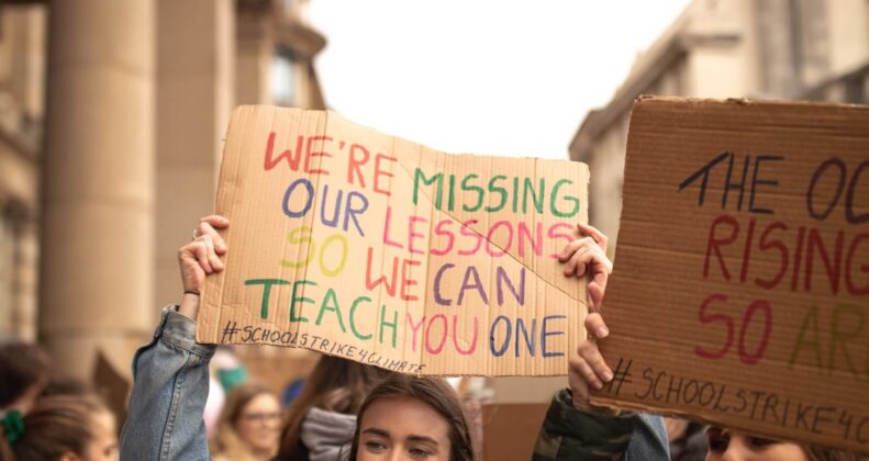 group of people raising cardboard box with text near building